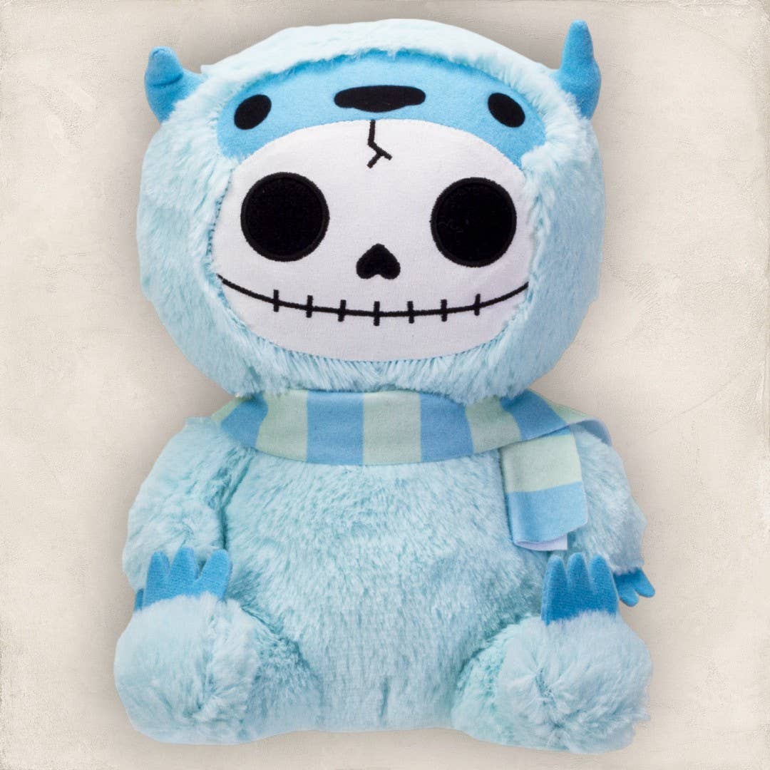 Blue furry plush with skull face and small horns wearing striped scarf.
