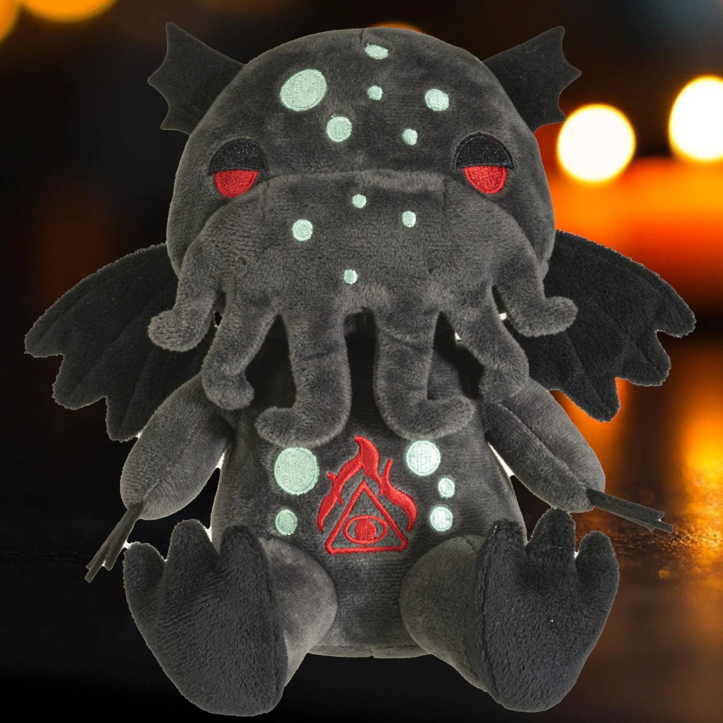 Dark gray plush Cthulhu with red eyes, light blue spots, tentacles, wings, and a red symbol on chest.
