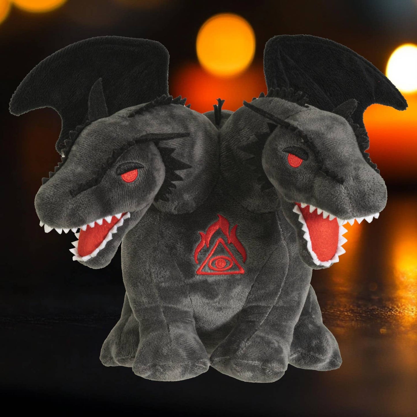 Dark gray double-headed dragon plush with red eyes and embroidered fiery symbol on chest.