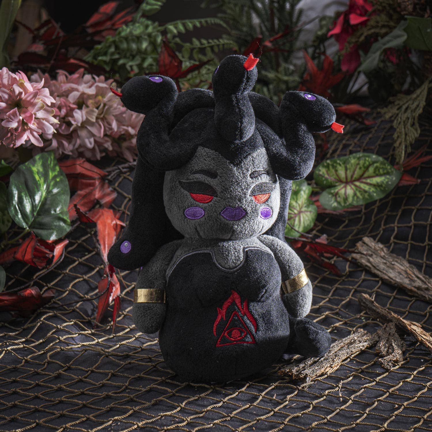 Black plush Medusa with red eyes, purple accents, and snake hair details sitting on mesh surface.