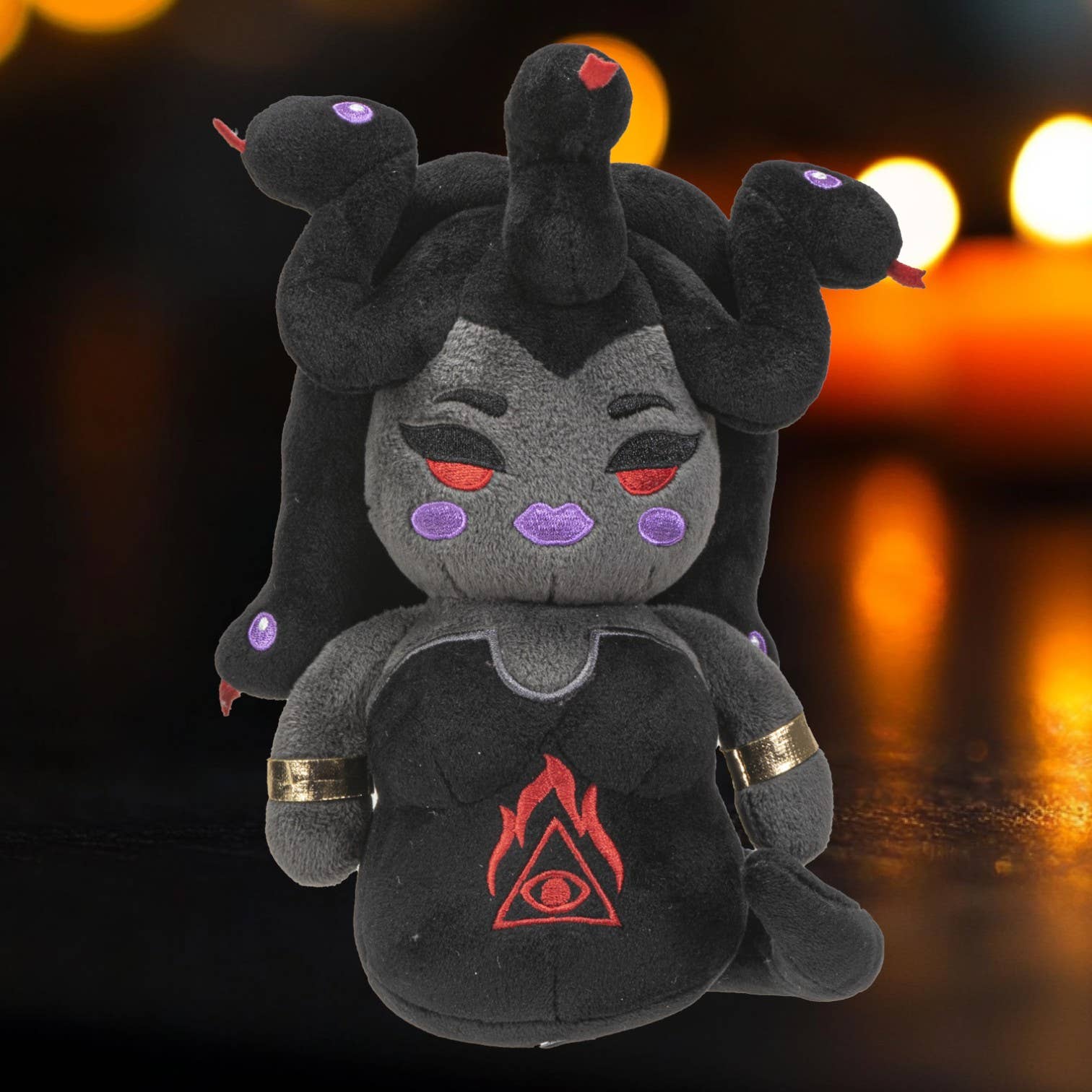 Dark gray plush inspired by Medusa with red and purple eye details and flame symbol on chest.